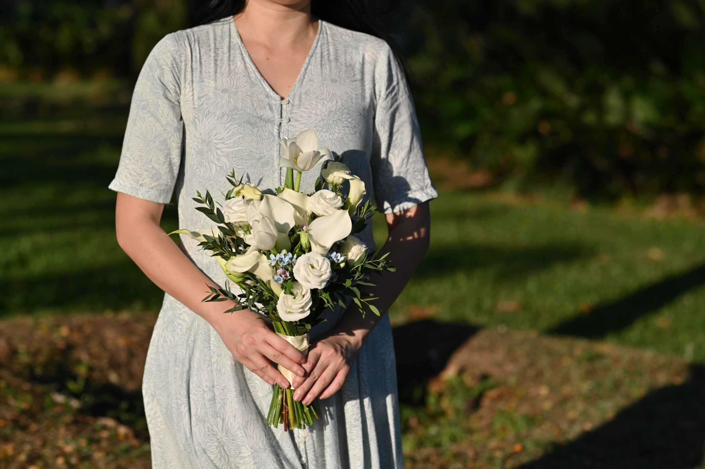 a girl holding bridal bouquet made with white calla lilies, tulips and blue oxypetalum